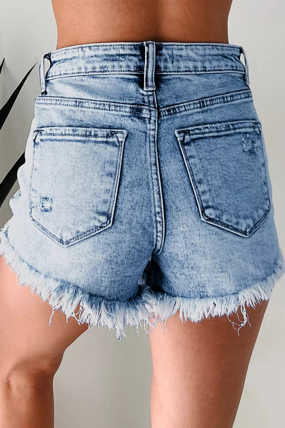 Medium wash distressed frayed hem denim shorts, back view