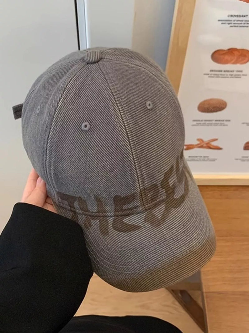 Dark gray cotton baseball cap with tonal lettering held in hand