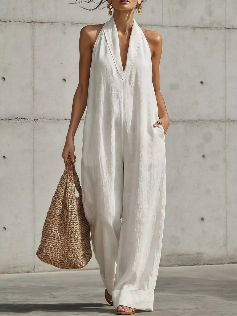 Halter neck wide leg jumpsuit worn with a woven shoulder bag and flat sandals