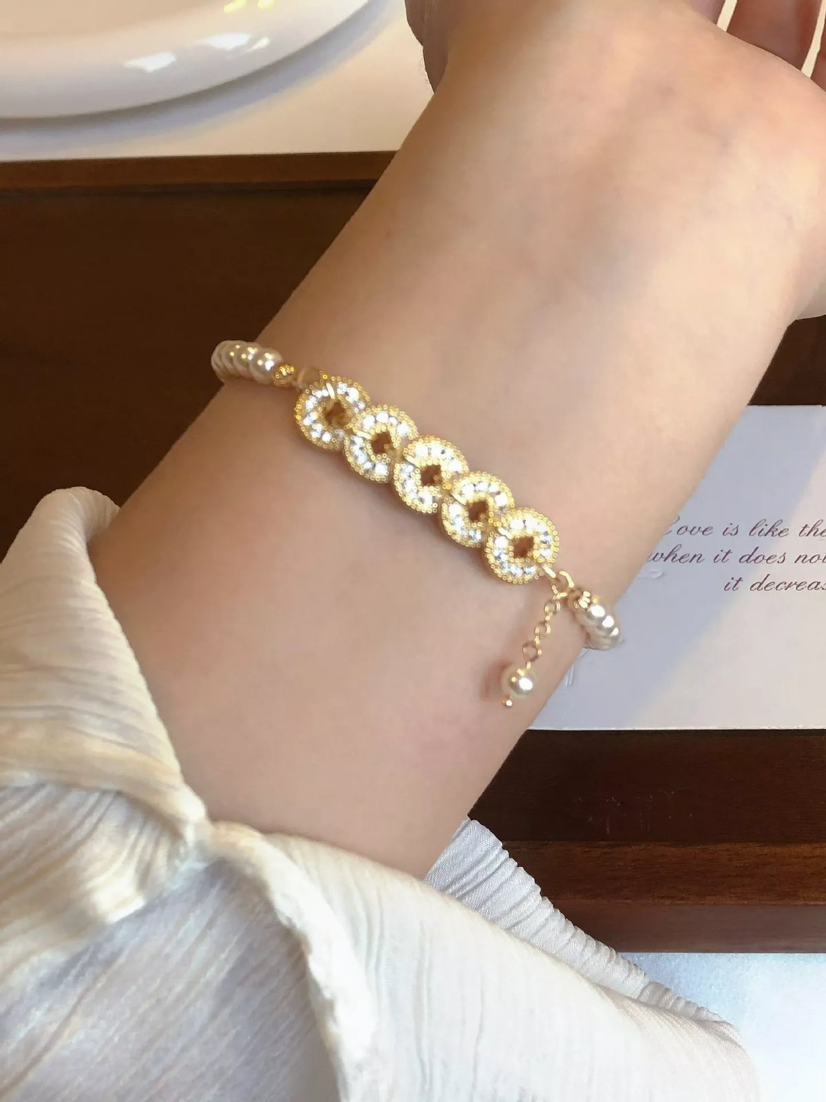 Gold plated pearl and coin charm bracelet on white background