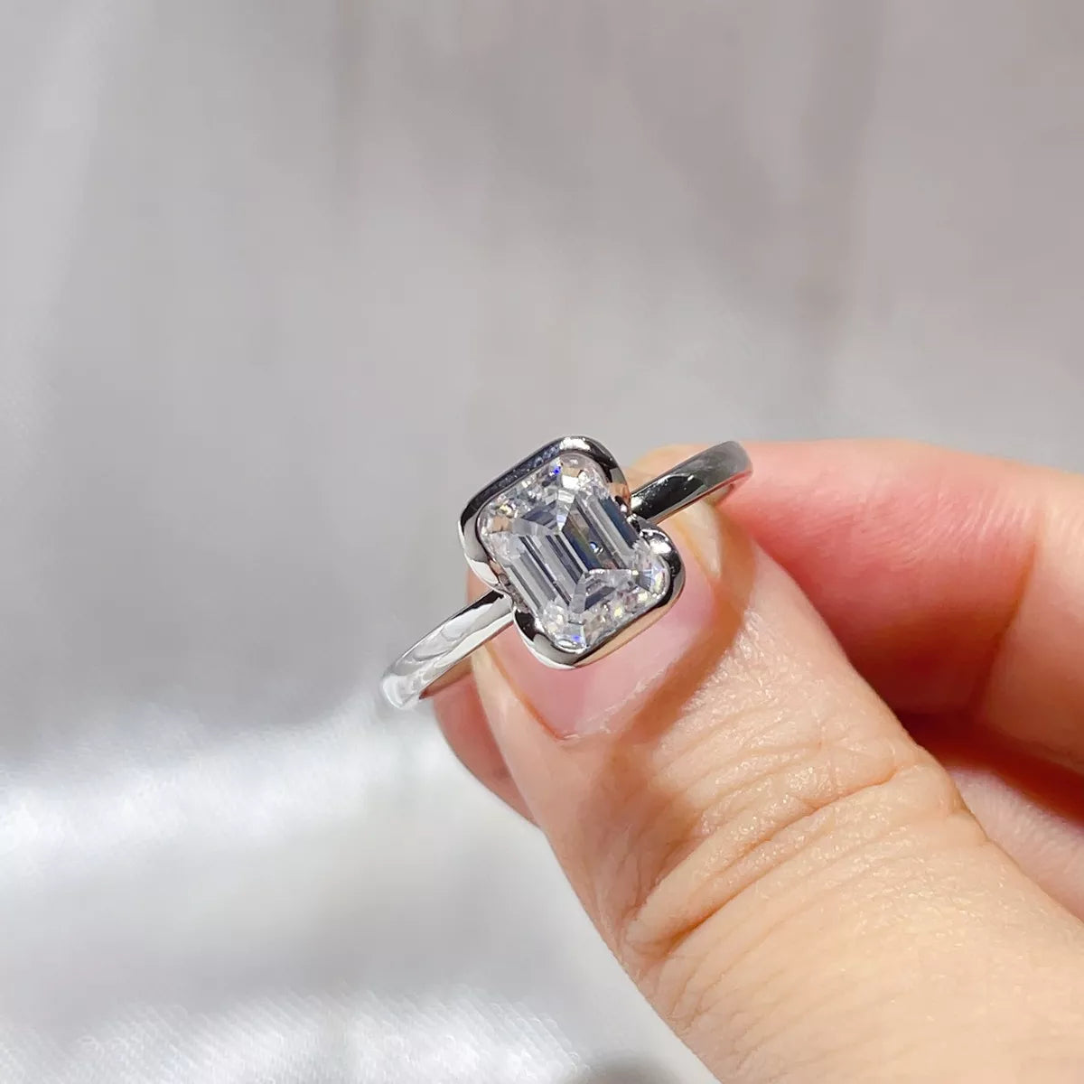 2 carat emerald cut moissanite ring in sterling silver held between the fingers