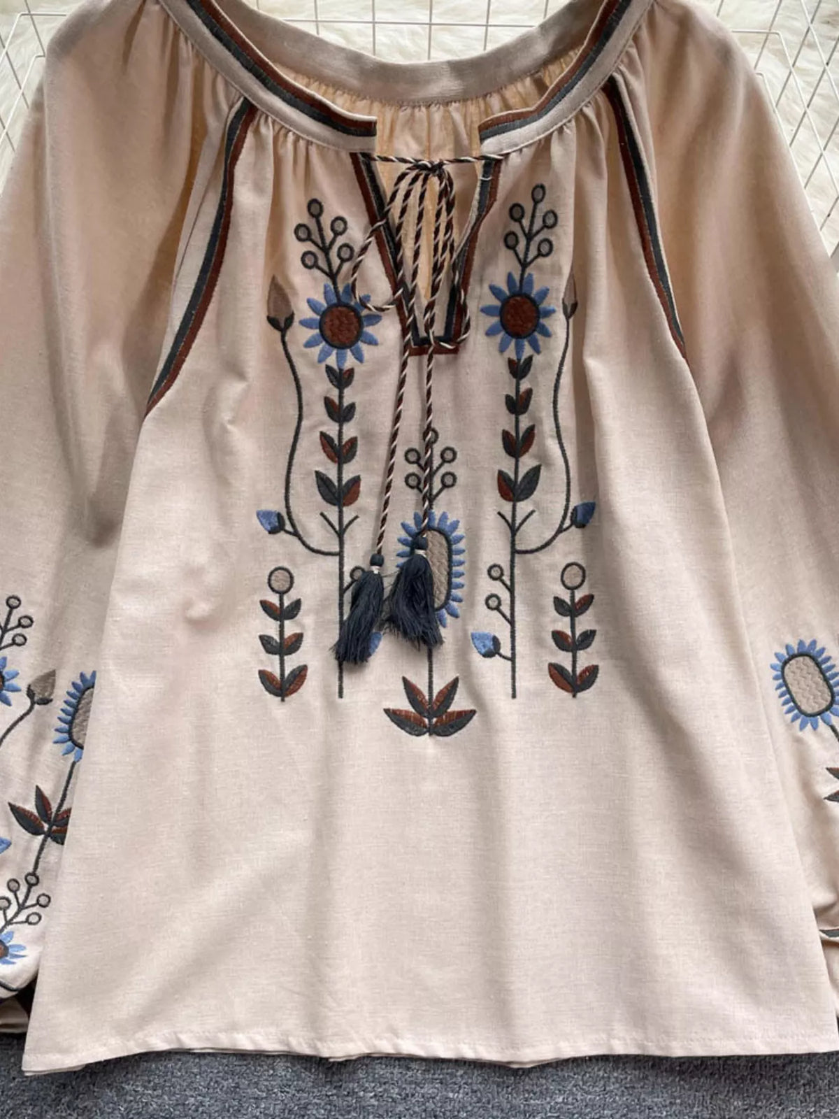 Tie neck with tassel ends on the embroidered blouse, close detail