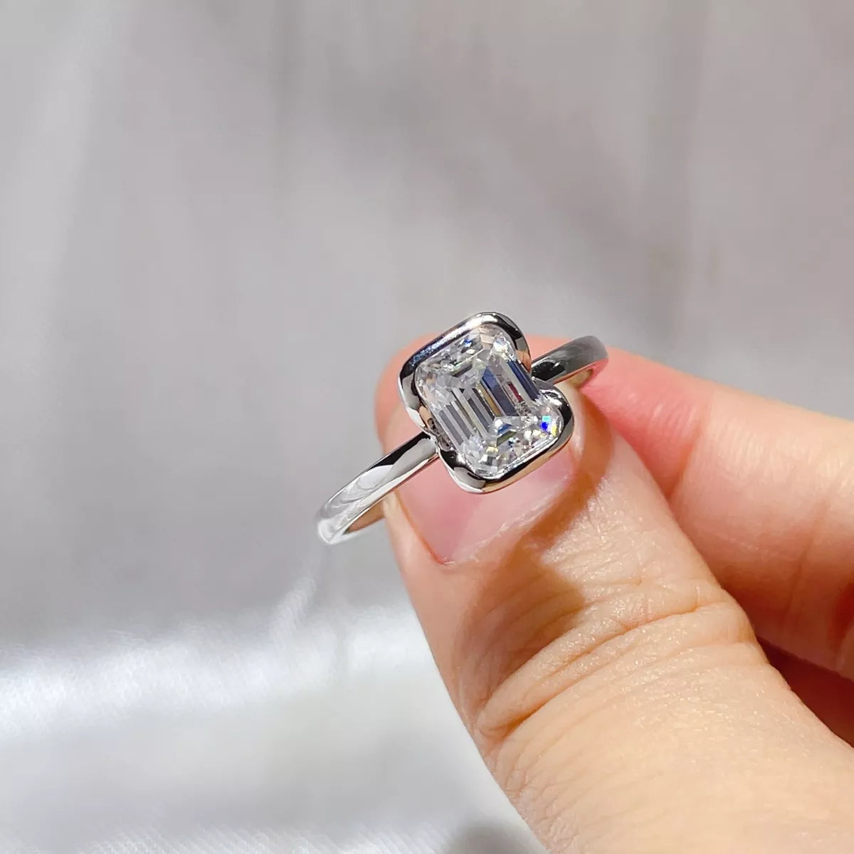 Emerald cut moissanite ring photographed against a soft fabric background